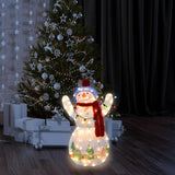 This is a lifestyle image showing the snowman sculpture lit up in front of a decorated Christmas tree in a living room.