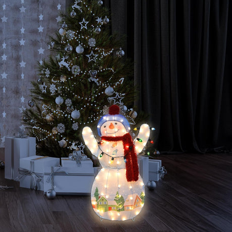 This is a lifestyle image showing the snowman sculpture lit up in front of a decorated Christmas tree in a living room.