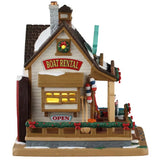 This is the other side of the building. There are signs that read "BOAT RENTAL" and "OPEN." There are oars and fishing rods leaning up against the wall. There are garlands and wreaths decorating the window and the deck.