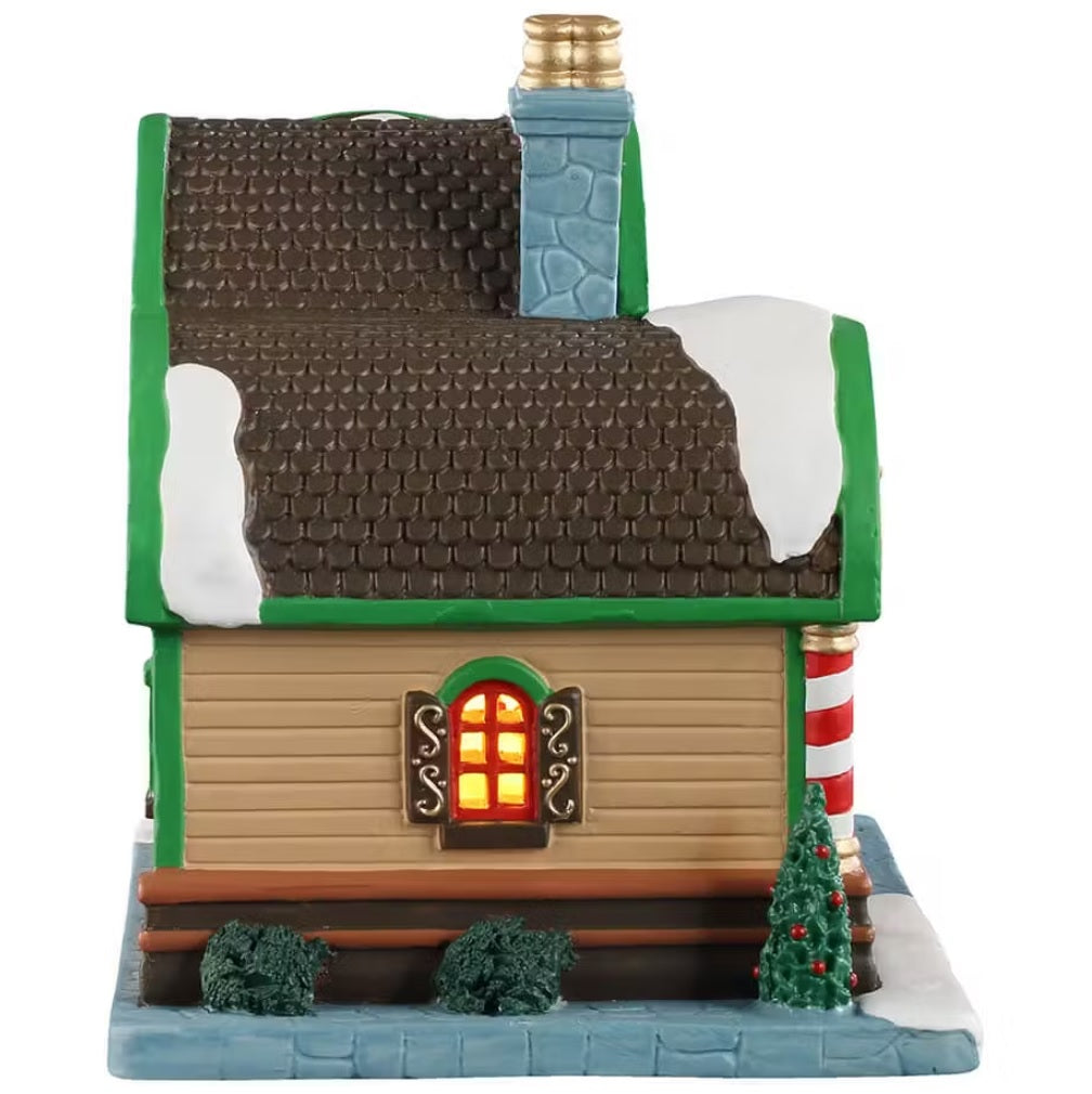 This is the other side of the building. There's a window with light shining through. There are two bushes and one decorated Christmas tree.