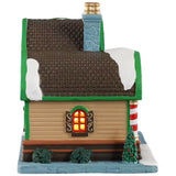 This is the other side of the building. There's a window with light shining through. There are two bushes and one decorated Christmas tree.