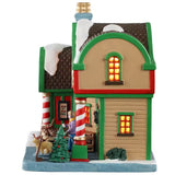 This is the side of the building. There are two windows with light shining through. There's a decorated Christmas tree near the front door. You can see the woman leaving with her dog.
