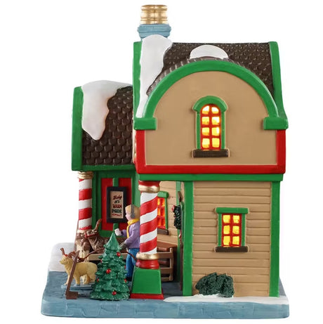 This is the side of the building. There are two windows with light shining through. There's a decorated Christmas tree near the front door. You can see the woman leaving with her dog.