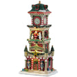 This is a Lemax lighted building designed to look like a clock tower decorated for Christmas. There are garlands and wreaths and decorated Christmas trees everywhere. On the second floor of the tower, there's a snowman, Santa and a polar bear standing on the balcony. On either side of the door, there are red and white striped columns and nutcrackers. There's snow on the roof and on the sidewalk.