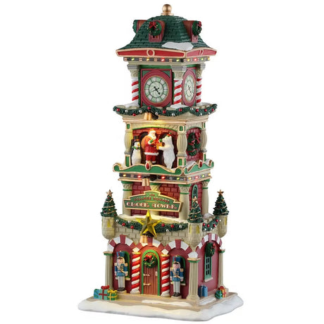 This is a Lemax lighted building designed to look like a clock tower decorated for Christmas. There are garlands and wreaths and decorated Christmas trees everywhere. On the second floor of the tower, there's a snowman, Santa and a polar bear standing on the balcony. On either side of the door, there are red and white striped columns and nutcrackers. There's snow on the roof and on the sidewalk.