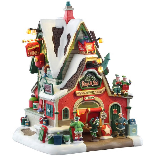 This is a Lemax lighted building designed to look like a shack turned into a sled repair shop. There's snow on the roof and on the sidewalk. There are elves eating lunch on the roof and elves working on a sled.