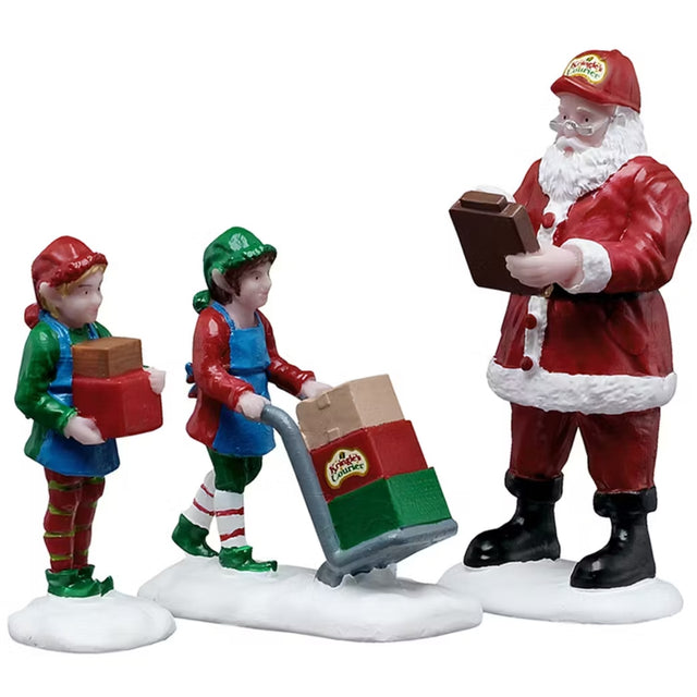 This is a set of three Lemax figurines designed to look like Santa checking his list while two elves are transporting different colored boxes. One elf is holding two boxes: one brown and one red. One elf is using a cart to move three boxes: one brown, one red and one green.