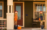 This is a lifestyle image showing the pumpkin press-in decoration in use. It's sticking out of a pumpkin on a porch. The porch is also decorated with two small scarecrows.