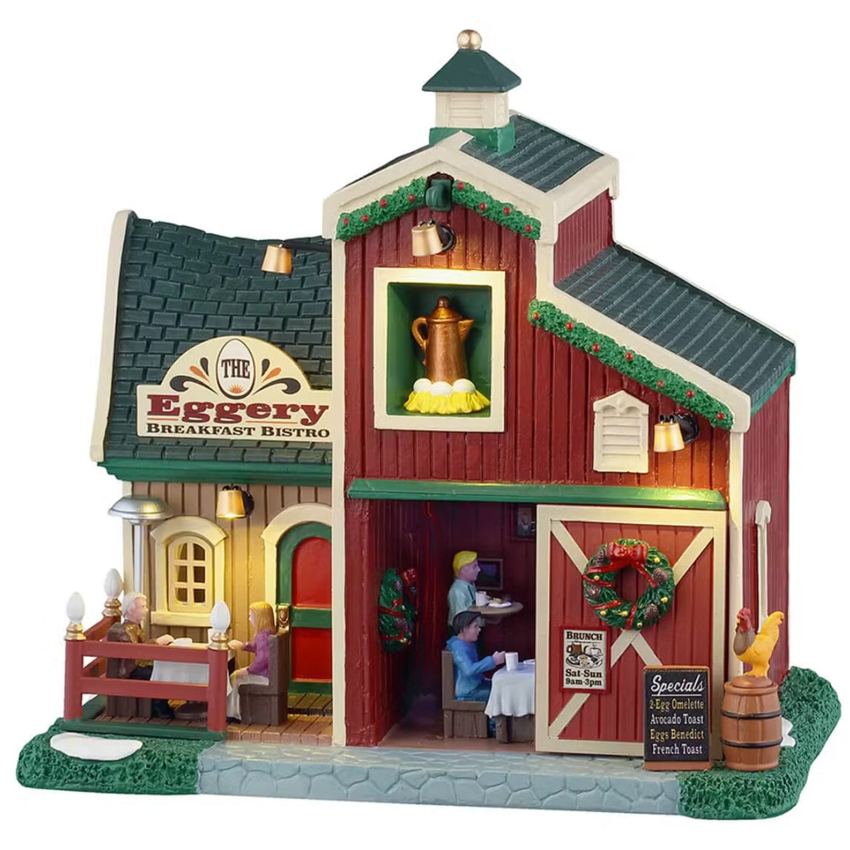 This is a Lemax lighted building designed to look like a barn turned into a breakfast restaurant. There are decorated garlands along the roof and a decorated wreath on the sliding barn door. There's a couple eating at a table on the balcony. Inside the building, there's a waiter bringing a table of people their breakfast. There's some snow on the grass.