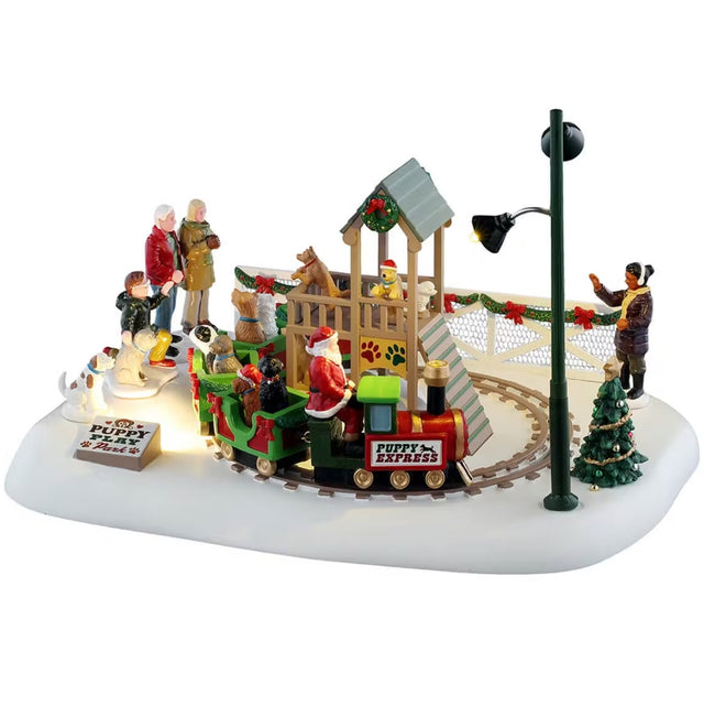 This is a Lemax table accent designed to look like a patch of land covered in snow. There's a small, circular train track with a Christmas-themed train going around it. There are dogs in each of the cars. Parents and other pets stand off to the side watching. 
