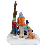 This is another view of this table accent. The boy is wearing a green winter hat and gloves, a red jacket, blue jeans and gray boots. The mom is wearing a purple winter hat, an orange jacket, gray pants and brown boots. The daughter is wearing a dark blue winter hat and gloves, a teal jacket, purple pants and light blue boots.