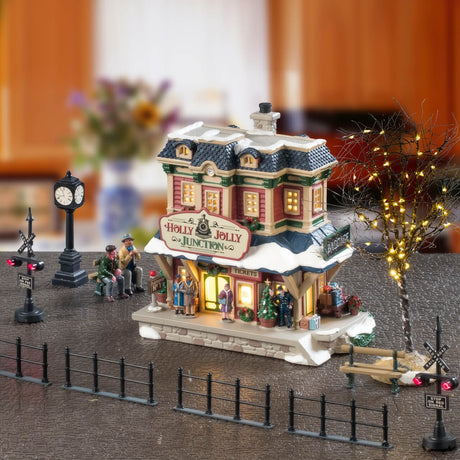 This is a lifestyle image showing this set on display. There's a train station, a clock, two benches, two sitting figurines, a bare tree, two railway stop lights, four pieces of canal fences, a light and two adaptors.