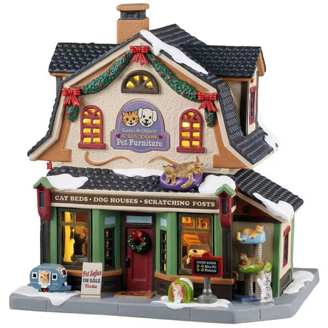 This is a Lemax lighted building designed to look like a cottage turned into a pet store. There's snow on the roof and on the sidewalk. It's decorated with garland, red ribbon and wreaths. On the sidewalk, there's a dog inside a house shaped like an RV and cats laying in a cat tower.