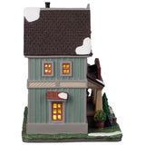 This is the side of the building. There's snow on the roof and on the front lawn. There are three windows on the side with lights shining through.