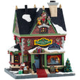 This is a Lemax lighted building designed to look like a tall, red, brick building. All over, there are stocking decorations with gingerbread cookies and peppermint candies sticking out. There's a window display of a snowman inside. There are wreaths and garlands and decorated trees. There are barrels with stuffed animals inside and a present on the sidewalk.
