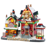 This is a Lemax lighted building designed to look like a string of two toy stores. There are small and large teddy bears everywhere. There are button accents and large spools of thread. There's a small machine full of fluff so you can create your own teddy bear.