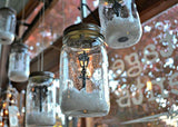 This is a lifestyle image showing some mason jars hanging as decorations. Inside the mason jars, there's faux snow and miniature lampposts.