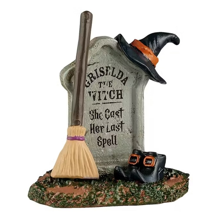 The tombstone reads "GRISELDA THE WITCH. SHE CAST HER LAST SPELL." There's a pointy witch hat resting on top and a broom and a pair of pointy shoes leaning up against it. 