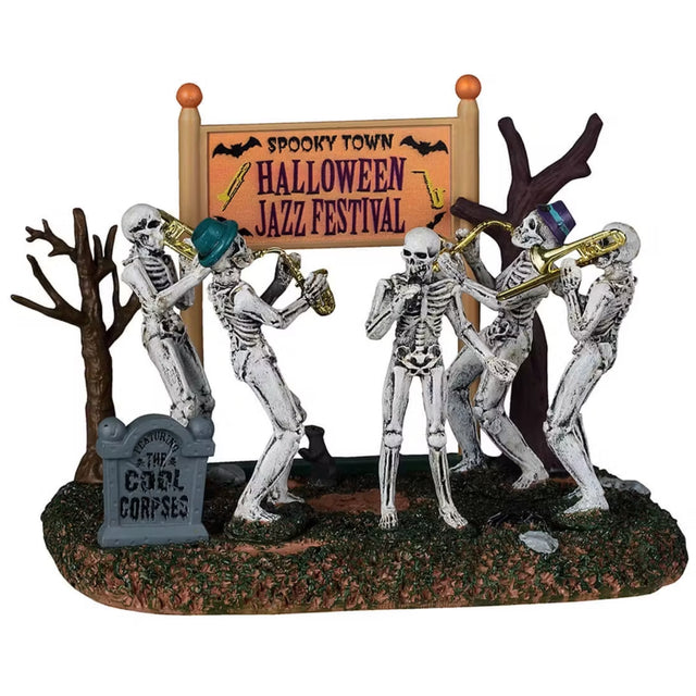 This is a Lemax Spooky Town table accent designed to look like a skeleton band playing instruments in between two dead trees. There's an orange sign behind them that reads "SPOOKY TOWN HALLOWEEN JAZZ FESTIVAL" and there's a sign on the ground designed to look like a tombstone that reads "THE COOL CORPSES."