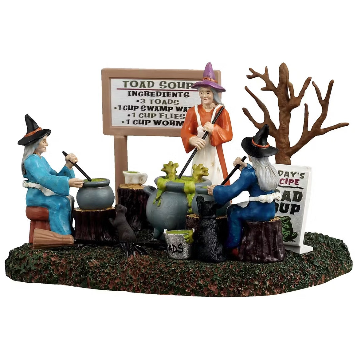 This is a Lemax Spooky Town table accent designed to look like three witches sitting around stirring their individual cauldrons. There's a white board that reads "TOAD SOUP. Ingredients: 3 toads, 1 cup of swamp water, 1 cup of flies and 1 cup of worms." One witch is sitting on a stool and is wearing a blue cloak with a black hat. One witch is sitting on a tree stump and is wearing a dark blue cloak with a black hat. One witch is standing up and is wearing an orange cloak with a pink hat.