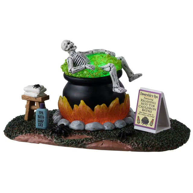 This is a Lemax Spooky Town table accent designed to look like a skeleton taking a bath in a big, black cauldron. The water glows green. There's a stool with a towel and a spider on it. Next to the cauldron, there's a tube of Spa Bath Soap. There's a sign next to the cauldron that reads "Esmeralda's Spa featuring Relaxing Hot Tub Cauldron Baths. But don't stay in the water too long!"