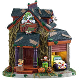 This is a Lemax Spooky Town lighted building designed to look like a rundown home. There are wooden boards all over the roof, vines growing all over and green slime everywhere. There's a sign above the front door that's shaped like a clown's head and it reads "THE LAFF SHAK." There's a bowl of candy on the front porch and jack-o-lanterns everywhere. Next to the garage door, there's a clown jumping out of a biohazard barrel. Inside the garage, there's a car with a clown head on the front bumper.