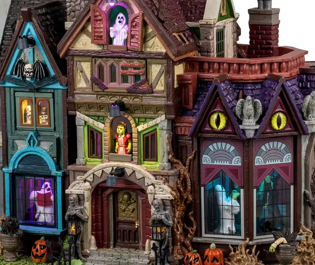 This is an up close view of this Lemax Spooky Town lighted building that's designed to look like a slightly dilapidated and very colorful mansion. Some of the accents include: skulls, jack-o-lanterns, owl statues and dead plants. There are ghosts, monsters and skeletons visible in the windows. 