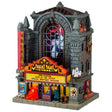 This is a Lemax Spooky Town lighted building that's designed to look like a tall, gothic building that's been turned into a movie theater. It's called Fright Night Cinema. There are ghosts visible through the big window in the front. Underneath the marquee, there are skulls and a vampire standing next to a werewolf.
