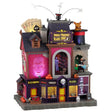 This is a Lemax Spooky Town Sights and Sounds building designed to look like a tall magic shop. On the roof, there are giant cards, a top hat with birds flying out of it and a giant orange rabbit in a giant top hat. There are magic tricks happening in every corner of the shop and an apparition of a man's head on the side of the building. 