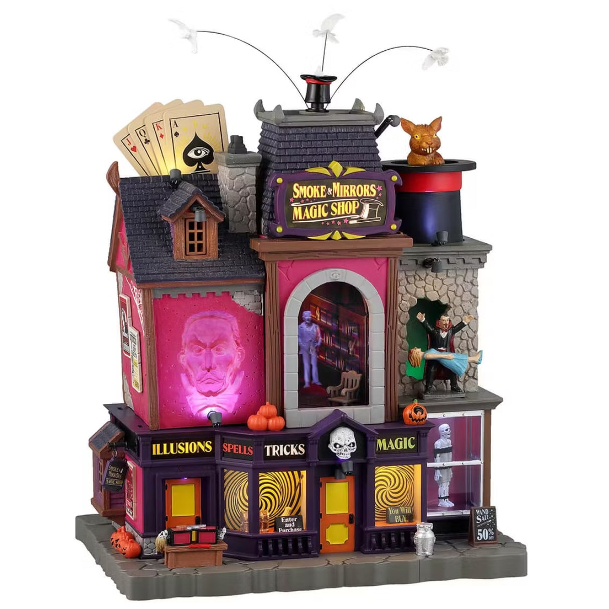 This is a Lemax Spooky Town Sights and Sounds building designed to look like a tall magic shop. On the roof, there are giant cards, a top hat with birds flying out of it and a giant orange rabbit in a giant top hat. There are magic tricks happening in every corner of the shop and an apparition of a man's head on the side of the building. 