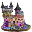 This is a Lemax Spooky Town building that's designed to look like a regal castle. It's decorated with skulls and bright lights. There are monsters up on the roof and near the moat. Inside the moat, there's a teal colored monster swimming toward two monsters in a boat.