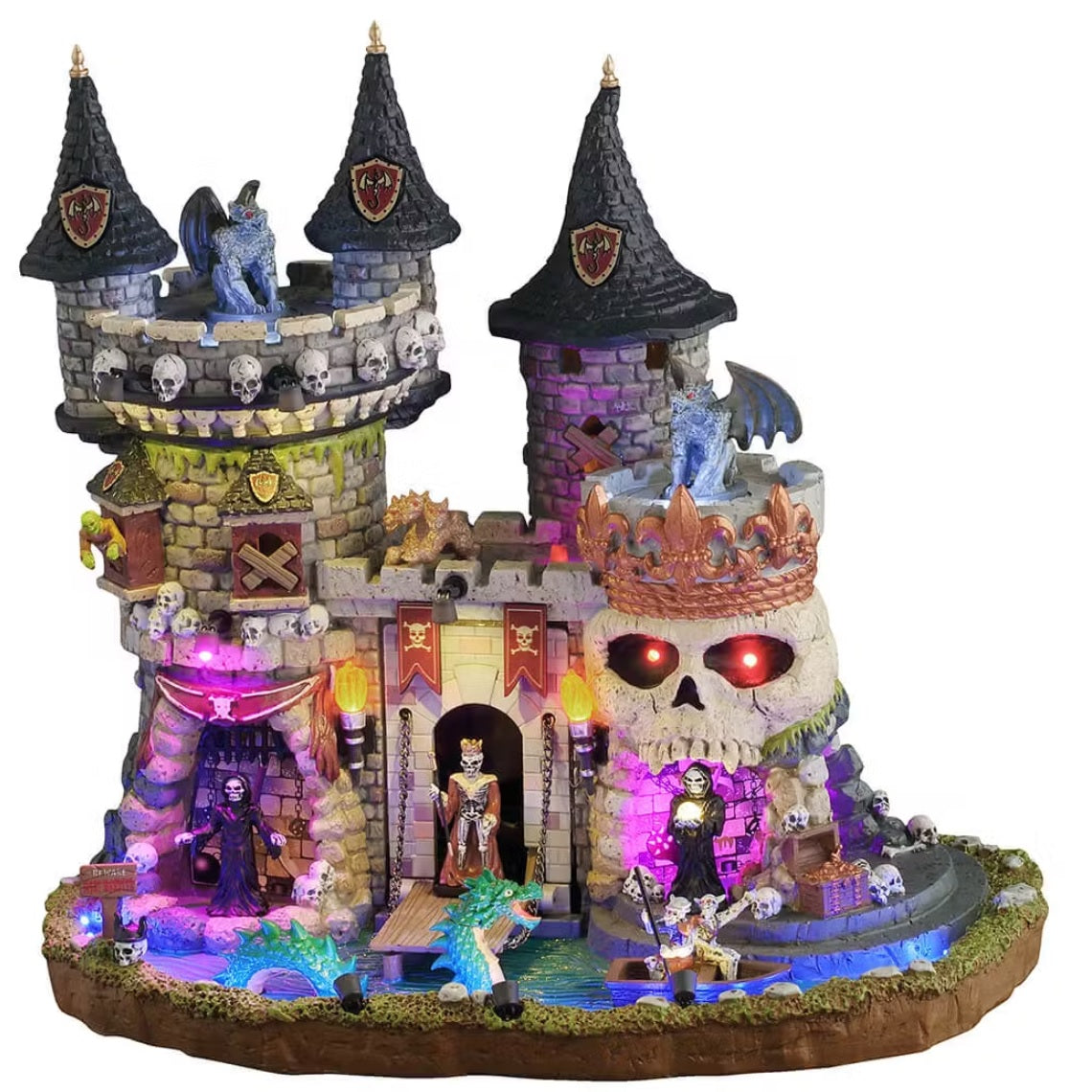 This is a Lemax Spooky Town building that's designed to look like a regal castle. It's decorated with skulls and bright lights. There are monsters up on the roof and near the moat. Inside the moat, there's a teal colored monster swimming toward two monsters in a boat.