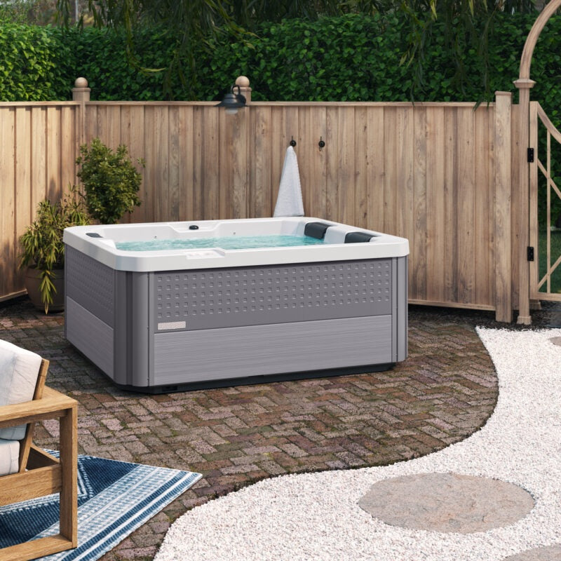 This is a lifestyle image of the hot tub on a brick patio next to a wooden fence.