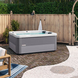 This is a lifestyle image of the hot tub on a brick patio next to a wooden fence.