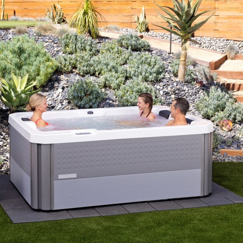 This is a lifestyle image showing three people inside this hot tub. The hot tub is in an exotic looking backyard.