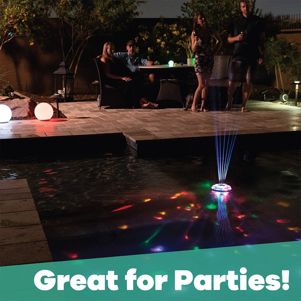 This is a lifestyle image showing the light show fountain floating in the middle of a pool while there are people partying alongside the pool.
