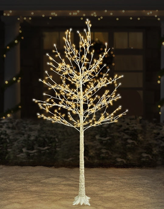 This is a lifestyle image showing the birch tree decoration on the snowy ground in front of a house. The lights are warm white and pure white.