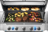 This is an up close view of food cooking on the grill. There are lemons and tortillas cooking on the top shelf. There are Brussel sprouts, corn on the cob, kebabs and two steaks cooking on the bottom shelf. 