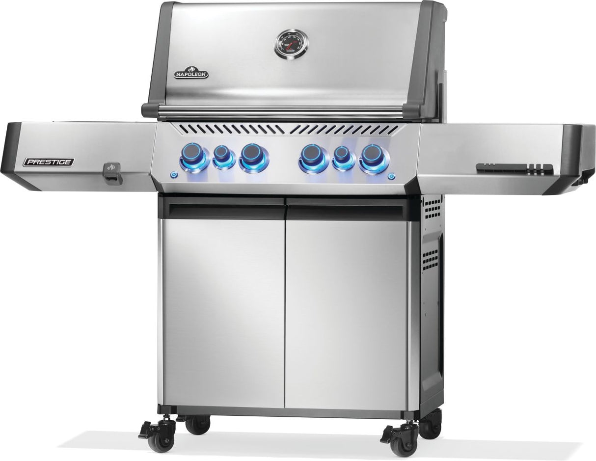 Silver and gray Napoleon grill. There is a built-in thermometer on the lid, there are two shelves outstretched, six buttons and a cabinet that opens up underneath. This is the right side view.