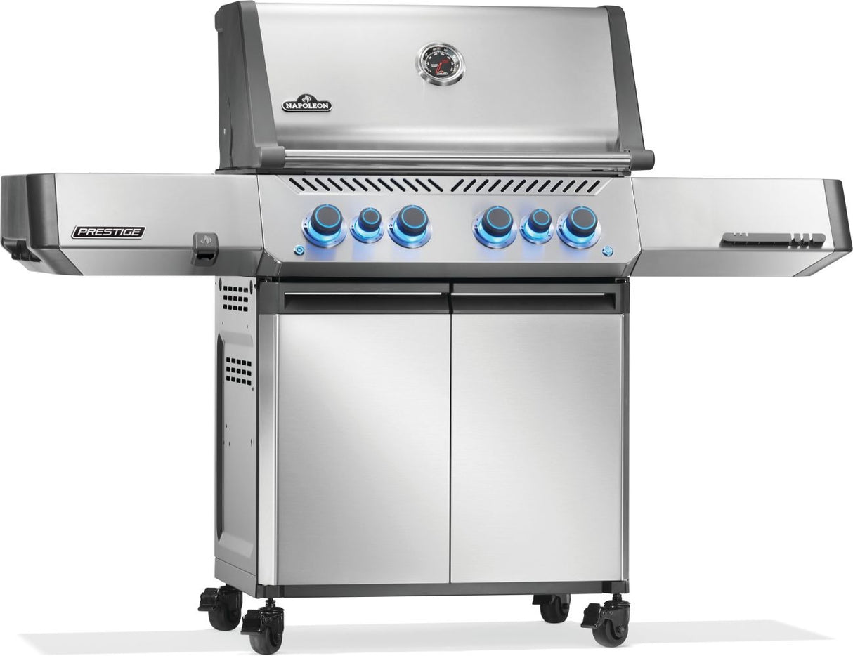 Silver and gray Napoleon grill. There is a built-in thermometer on the lid, there are two shelves outstretched, six buttons and a cabinet that opens up underneath. This is the left side view.