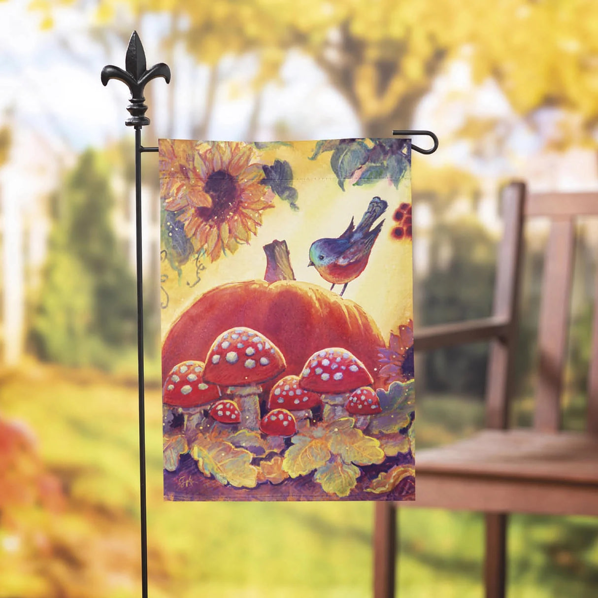 Yellow flag that features a sunflower, leaves, mushrooms, a large pumpkin and a blue bird sitting on the pumpkin.