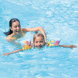 This is a lifestyle image showing a young girl swimming with the arm bands on it while her mom helps from behind.