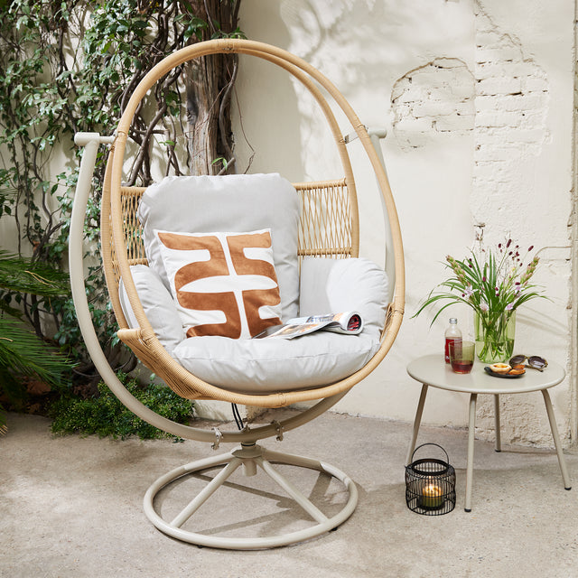 This is a lifestyle image of the swivel egg chair in beige. It's next to a small table and some plants.