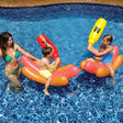 An inflatable ride on pool game. The pool floats are shaped like hot dogs in buns. The battle boppers are shaped like condiments. One is ketchup and one is mustard. This image shows children on the hot dogs battling in the pool while their mom watches.