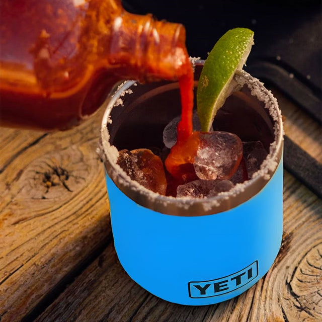 Blue colored lowball Yeti cup. This is a lifestyle image showing someone making a Bloody Mary drink inside of the cup.