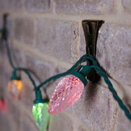 This is a lifestyle image showing one of the clips resting on a brick and it's holding a string of lights.