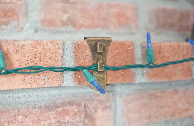 This is a lifestyle image showing one of the clips resting on a brick and it's holding a string of lights.