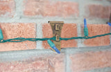 This is a lifestyle image showing one of the clips resting on a brick and it's holding a string of lights.