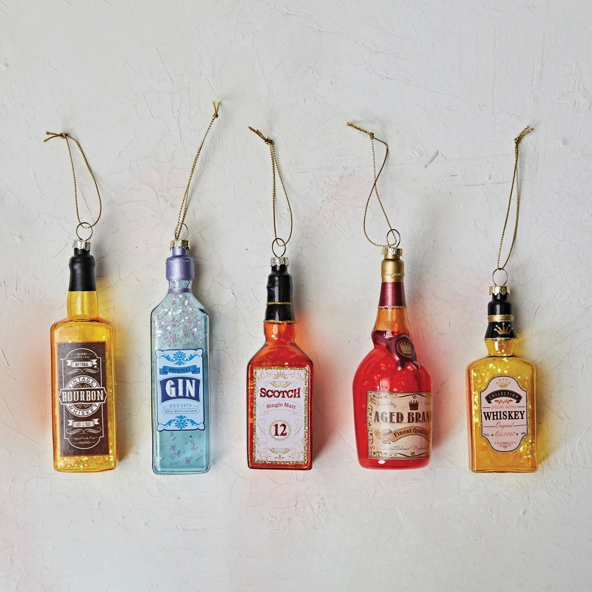 Ornament shaped like a miniature bottle of alcohol. One ornament is red and reads "Aged Brandy." One ornament is yellow and reads "Whiskey." One ornament is orange and reads "Scotch." One ornament is yellow and reads "Bourbon." One ornament is light blue and reads "Gin." Each ornament has glitter inside.