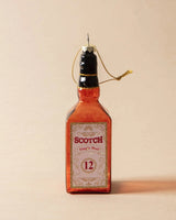 Ornament shaped like a miniature bottle of alcohol. One ornament is red and reads "Aged Brandy." One ornament is yellow and reads "Whiskey." One ornament is orange and reads "Scotch." One ornament is yellow and reads "Bourbon." One ornament is light blue and reads "Gin." Each ornament has glitter inside.